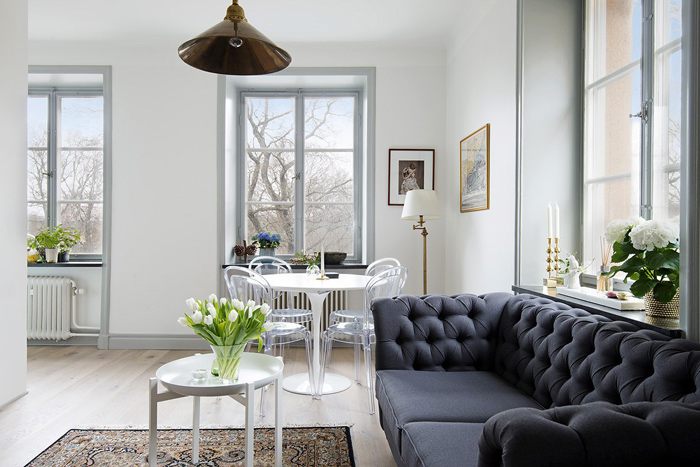 Granatowa pikowana sofa,biały okragły stół z przeźroczystymi nowoczesnymi krzesłami,stolik z tacą