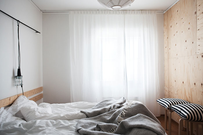 Żarówka w fabrycznej oprawie z amocowana na relingu nad łóżkiem w skandynawskiej sypialni