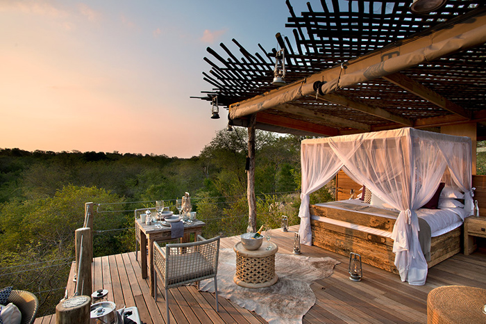Drewniane łóżko ze skrzyniami, firanymi z muślinu,drewniane stoliki z bambusowymi fotelami,skóry na podeście tarasu w afrykanskim stylu