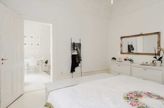 Biała sypialnia ze złotym lustrem nad komodą