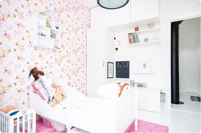 Tapeta w kwiatki, różowy dywanik,białe łózko w dziecięcym pokoju dla dziewczynki