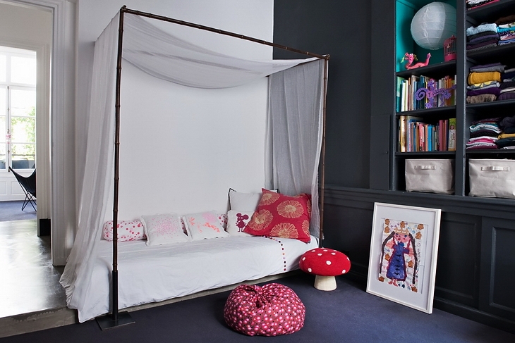 Nietypowy pokój dziecięcy z łóżkiem z baldachimem, grafitowym regalem z półkami i różowymi dodatkami