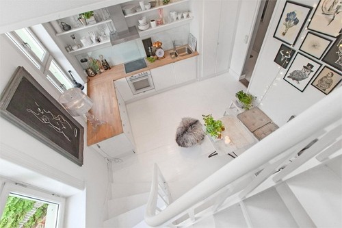 Widok z góry na biała kuchnię z drewnianymi blatami,biała podłogą i biało-czarnymi fotografiami i grafikami