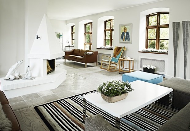Biały salon z kominkiem,kamienną nowoczesna podłogą,skórzaną sofą i nowoczesnym stolikiem na pasiastym dywanie