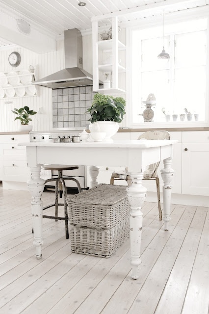 Bielone deski na podłodze,wiklinowe walizki i tradycyjny biały stół z drewna w stylu skandynawskim w kuchni