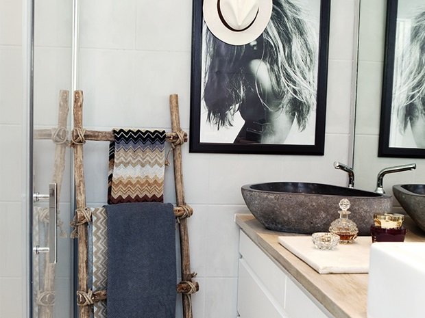 Kamienna szara umywalka w białej łazience z czarno-bialymi fotografiami i rustykalną drabiną z drewna