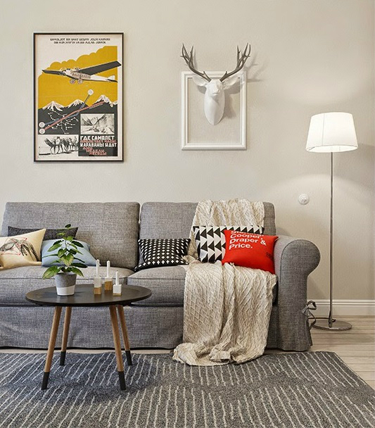 Skandynawski okragły stolik na drenianych nóżkach z czarnym blatem,szara sofa,plakaty i biały jelonek na ścianie