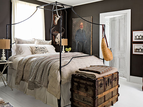 Czarne ściany, kute łóżko i kufer podróżnika w sypialni