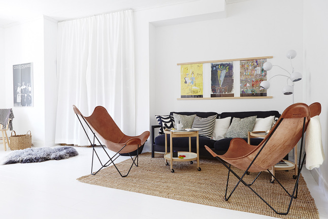 Beżowy dywan,czarno-białe poduszki,czarna sofa,brązowe fotele butterfly i drewniany stolik w aranżacji salonu z białą podłoga i ścianami