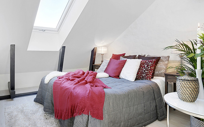 Biała sypialnia z szarą narzutą i różowymi poduszkami i pledem