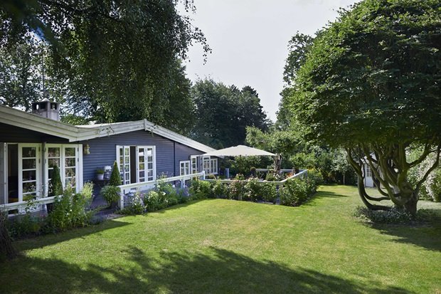 Piękny skandynawski dom z szarą elewacją,białymi oknami i płotem, z rozległym zielonym ogrodem i tarasem