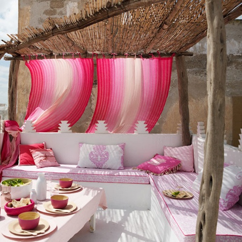 Różowe zasłony, różowe poduszki  i różowa zastawa w aranżacji letniego tarasu