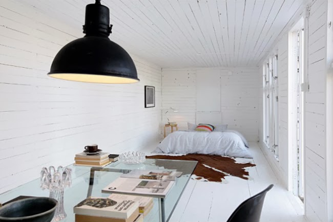 Biała sypialnia z czarną industrialną lampą,szklanym stołem i dywanem z byczej skóry
