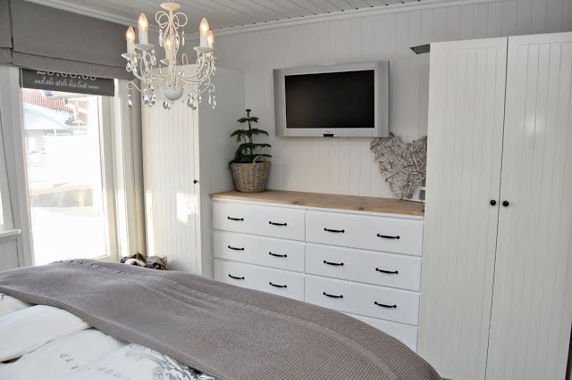 Żyrandol, białe szafy z komodami w sypialni w stylu skandynawskim