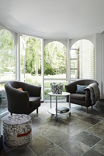 Szara kamienna płytka na podłodze,nowoczesne szare fotele,okragły stolik na kółkach w salonie z łukowanymi oknami w wykuszu