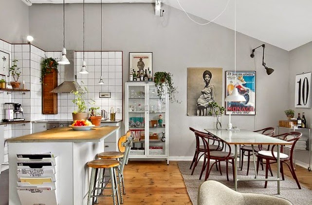 Kuchnia z jadalnią z plakatami i fotografiami na ścianie, biała gablotą,oldchoolpwymi krzesłami,drobnymi meblami vintage i z industrialnymi lampami