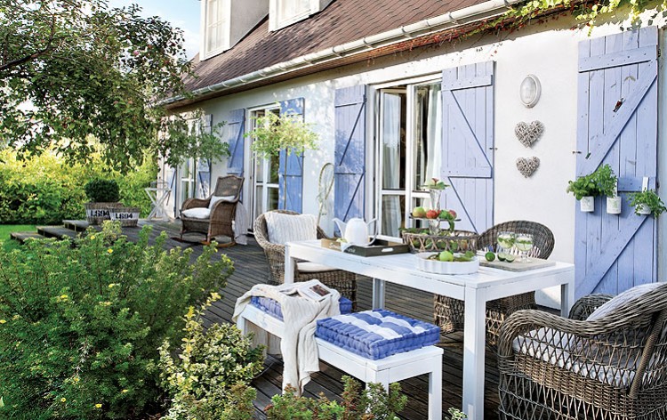 Niebieskie okiennice w białym domku  z pięknym drewnianym tarasem