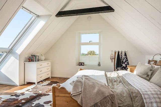 Biała sypialnia pod skośnym dachem,dywana ze skóry bydlęcej,biała komoda i drewniane łóżko