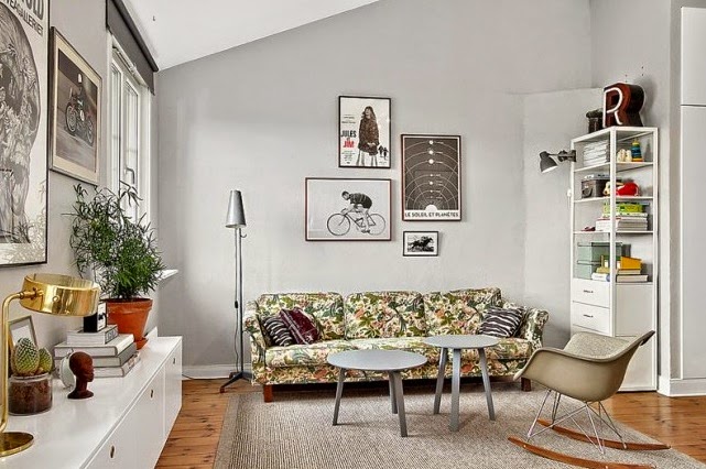 Szare okrągłe stoliki kawowe,fotel na płozach,kwiecista sofa i oryginalne grafiki na szarych ścianach w salonie
