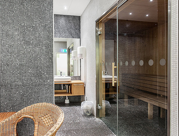 Mała sauna z prysznicem w aranżacji biało-czarnej łazienki z wiklinowym fotelem i drewnianymi meblami