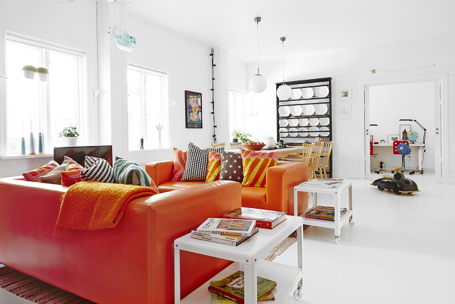 Pomarańczowe sofy ze skóry,białe stoliki pomocnicze,czarny regał z pólkami i biała podłoga w salonie