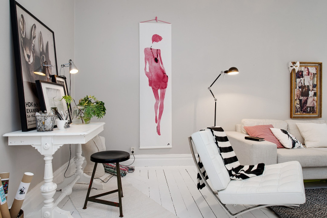 Biało-różowy plakat i złocone ramy na ścianie w białym salonie z drewniana konsolką i czarnymi dodatkami