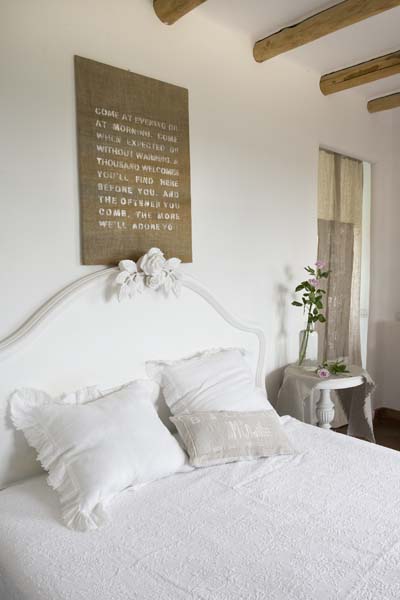 Białe rzeźbione łóżko w sypialni z drewnianymi belkami