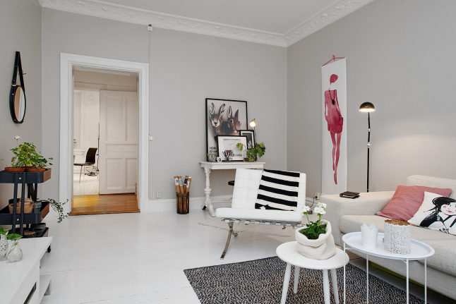 Biała konsolka i białe fotele z sofą w skandynawskim salonie z różowym plakatem i różowymi poduszkami