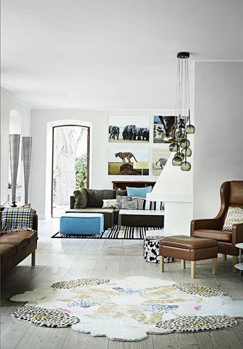 Nowoczesny biały salon ze szklanymi lampami,skórzanymi brązowymi meblami,dizajnerskimi dywanami i turkusowa pufą