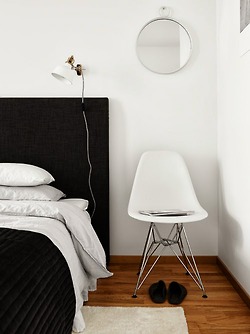 Czarne tapicerowane łóżko,czarna narzuta,okragłe srebrne wiszące lusterko i drewniana podłoga w miodowym kolorze
