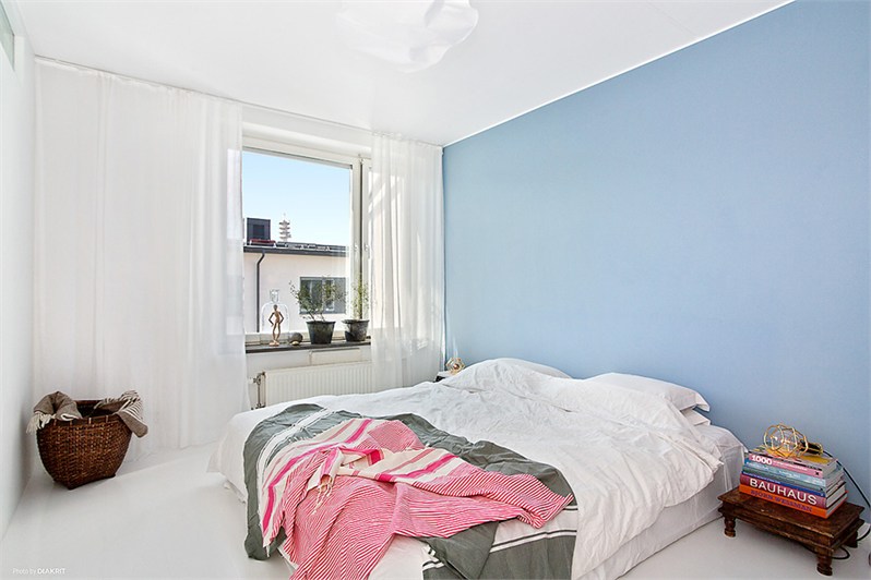 Biała sypialnia skandynawska z jedną niebieską ścianą przy łóżku