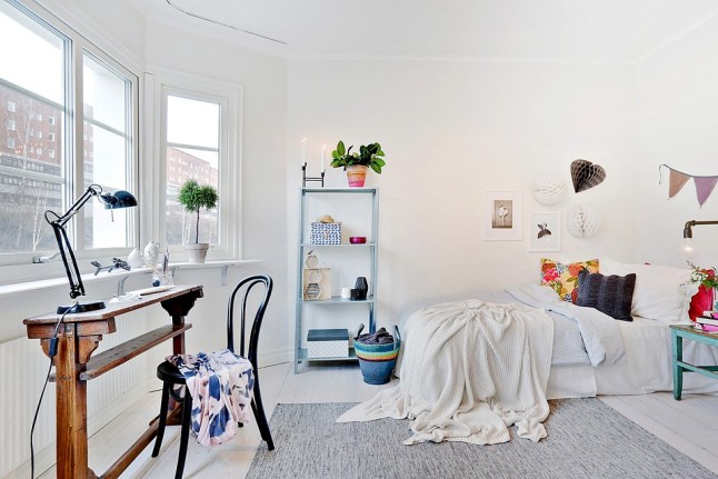 Niebieska drabina z półkami,turkusowy stołek,drewniana konsolka,szary dywan i niebieskie dodatki w białej sypialni