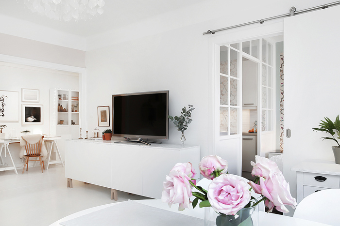 Przesuwne białe drzwi w salonie skandynawskim z kącikiem tv i biurkiem