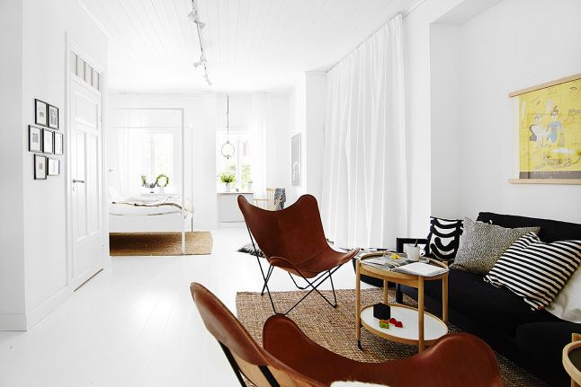 Czarna sofa,brązowe fotele butterfly i drewniany stolik w aranżacji salonu z białą podłoga i ścianami