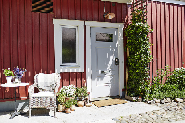 Czerwona elewacja skandynawskiego domu z szarymi drzwiami i małym ogródkiem przed domem