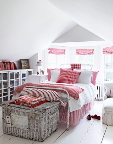 Biały wiklinowy kufer, przeszklone komody i czerwono-biała pościel w białej sypialni na poddaszu