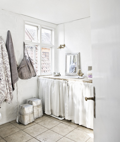 Romantyczna wiejska łazienka w bieli z bawełnianymi fartuchami przy szafkach