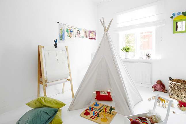Biały pokój dziecięcy z namiotem tippi,tablica na drewnianym stojaku i żólto-turkusowymi poduszkami