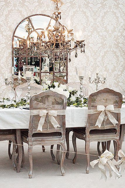 Prowansalski żyrandol z paciorkami,francuskie ozdobne świeczniki na światecznym stole,francuskie dzielone lustro i prowansalskie krzesła bielone z rattanowymi oparciami przewiązanymi białymi wstążkami