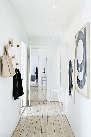 Podłoga olejowana z naturalnego drewna,drewniane wieszaki ścienne grzybki,białe ściany,nowoczesne czarno-białe grafiki na ścianie w wąskim przedpokoju