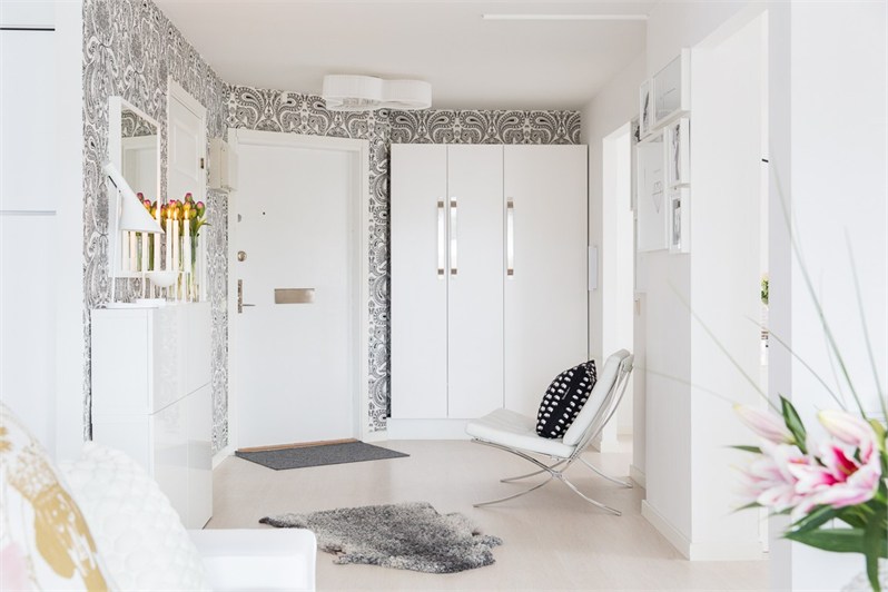 Białe nowoczesne szafy w aranzacji przedpokoju z biało-czarną tapetą z ornamentem,nowoczesny fotel na chromowanych nogach