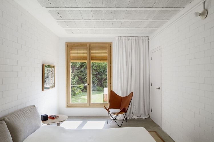 Ściany z białej cegły i fotel butterfly ze skóry w białej sypialni skandynawskiej
