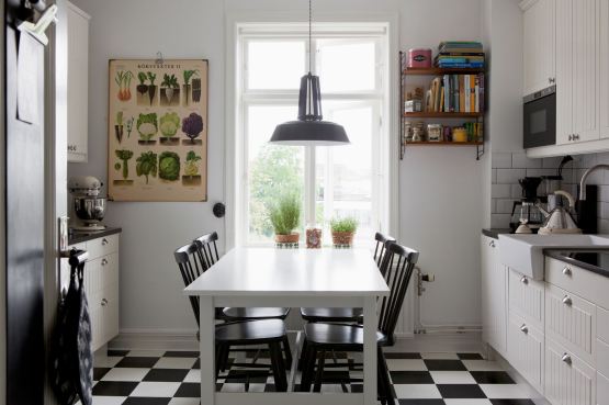 Biało-czarna terakota ułożona w karo w białej kuchni z białym stołem, czarnymi krzeslami i plakatem z ziołami