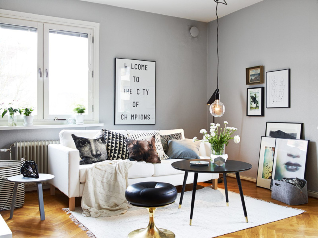 Szare ściany, żarówka na kablu,czarny okragły stolik,gafiki i typografie i drukowane poduszki w salonie skandynawskim