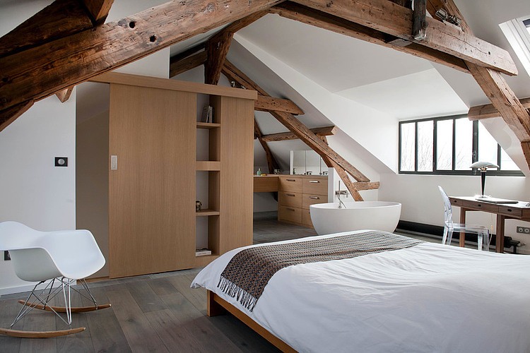 Owalna wanna w biało-brązowej sypialni z drewnianymi belkami i nowoczesnymi krzesłami