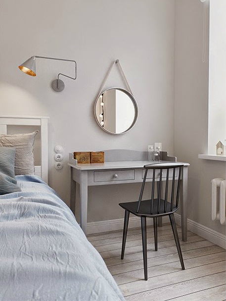 Szary kinkiet nowoczesny , okrągłe lustro na rzemyku,szara toaletka z grafitowym krzesłaem w sypialni z białym łóżkiem