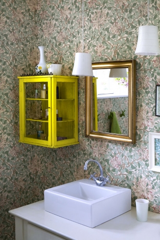 Kwiecista tapeta,żółta szafla i złote lustro w łazience