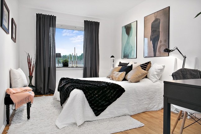 Nowoczesne artystyczne fotografie na ścianie w białej sypialni z czarnymi zasłonami,biurkiem i futrzaną narzutą